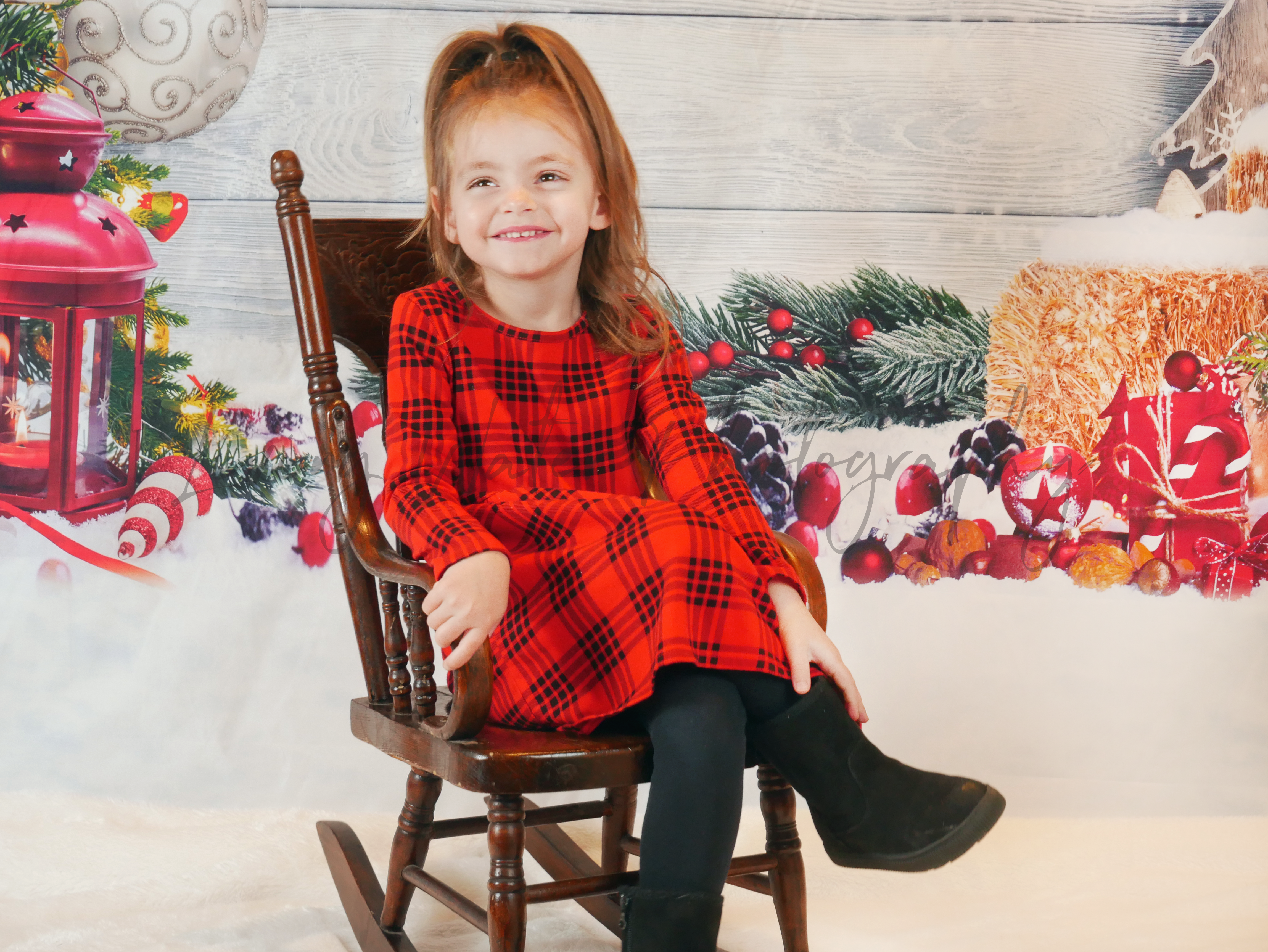 Young girl smiling in rocking chair with festive Christmas studio backdrop
